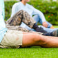 Two men sitting on grass with one wearing a camouflage jacket