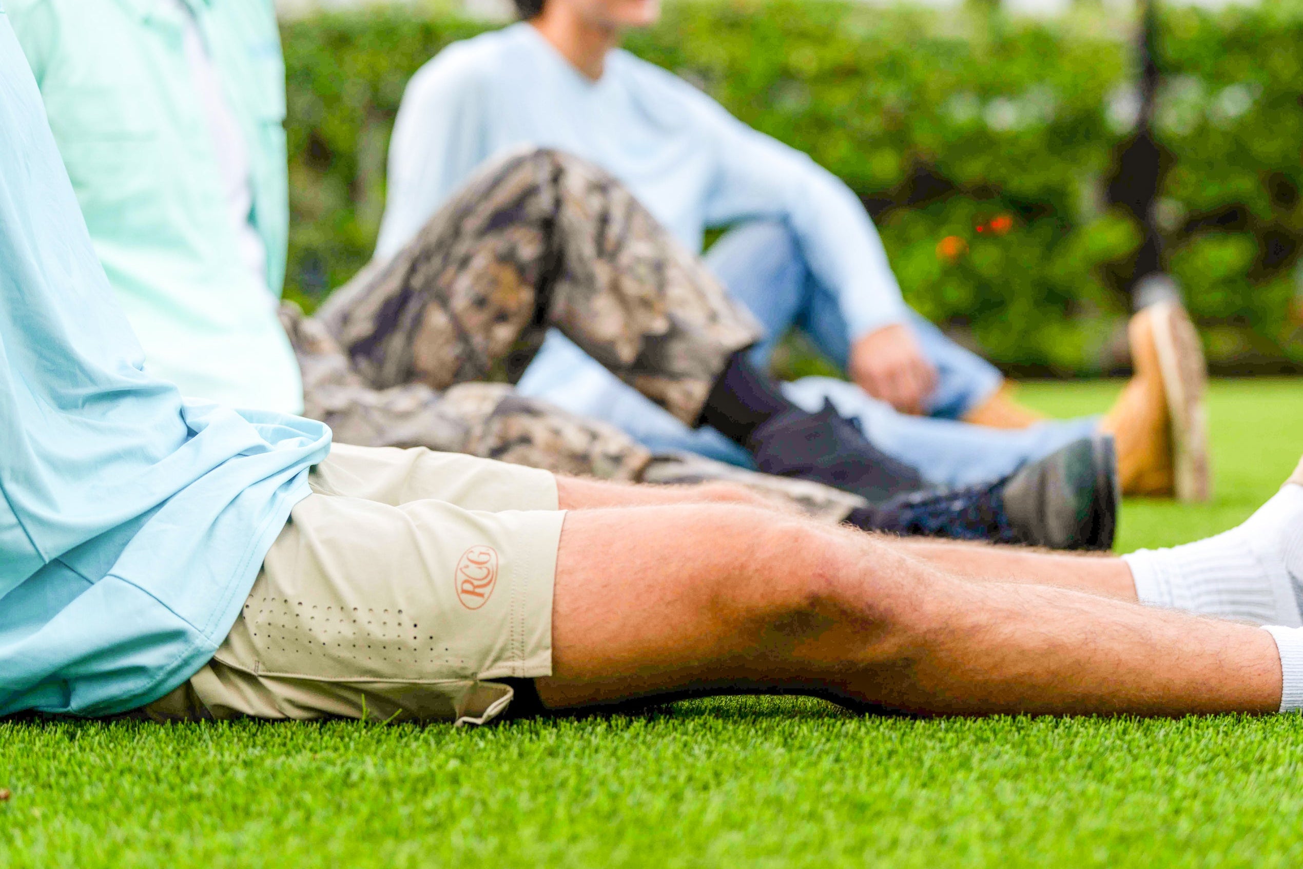 Two men sitting on grass with one wearing a camouflage jacket